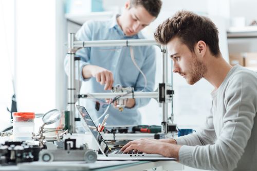 Young man working on laptop and young man building invention.